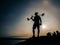 Guy with a metal detector stands against the backdrop of a beautiful sunset on the coast. Silhouette of a man with a shovel and a