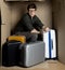 Guy is posing in cramped carton room with his luggage