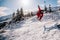 A guy in a red jumpsuit jumps on a snowboard from a snow ledge