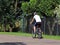 The guy rides on the back wheel of a bicycle on the asphalt road in the village against the backdrop of a football field. Ecologic