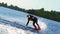 Guy rushing along forest lake on wakeboard touching water surface by hand