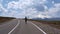 The guy in the shorts and t-shirt barefoot running on empty highway on a background of beautiful clouds and mountains. Elbrus