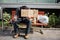 Guy is sitting on bench and holding a cardboard with help word on it. Also he has a cup with dollar bill in right hand