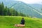 Guy sitting on log and enjoy peaceful green mountains landscape. Peace of mind and relax