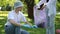 A guy, squatting, collects garbage scattered on the grass in the park and puts it in a plastic bag, which is held in the