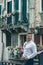 Guy on the street in venice in looking back a white shirt against the background of venetian balconies with flowers Venice