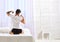 Guy stretching arms, full of energy in morning, rear view. Perfect morning concept. Man in shirt sits on bed, white