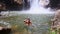 Guy swims near waterfall foamy base in pond among rocks