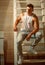 Guy in trendy tank top and jeans fashion. Young man sit on ladder. Athletic macho with muscular chest and hands. Fashion