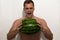 The guy is trying to crush a huge watermelon in his hands. A guy with a bare torso on a light background