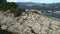 Guy waves hand sitting on grey rock on stone cliff cape