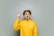 A guy in yellow clothes stands on a background of a gray wall with his fingers raised and has ideas, looks up and smiles