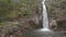 Guys Swim by High Waterfall in River in Tropical Park