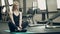 In the gym, a beautiful woman sits in a lotus position and rests.