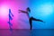 Gymnast woman stretching in front of brick wall in neon lights. Flexible muscular woman doing spirals with ribbon.