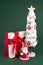 Gypsum colorful santa claus on the gift box and christmas tree with decorations over green background. Copy space