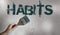 Habits Sign Painted and a hand holding paintbrush on light grey wall background. Bad habits addiction concept