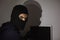 Hacker in balaclava hacking laptop while looking at camera