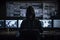 Hacker dressed in a hoodie, sitting in a dark room surrounded by monitors, coding malicious software. Ai generated