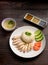 Hainanese chicken rice with soup and three sauces on dark wood table texture close up