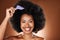 Hair care, beauty and black woman with comb in afro smiling in studio on brown background. Fashion, hair salon and face