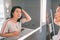 Hair loss mature Asian woman touching her hair styling or coloring gray hair looking at herself in home mirror