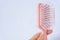 Hair loss problems with hand holding a pink hairbrush on white background. Falling black hair clinging to the comb