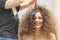 The hair master makes a hairstyle for a woman. Portrait of a beautiful Caucasian girl with flowing curly hair. The