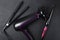 Hair master`s equipment on the black background.Top view of dark professional hair dryer, curling iron, straightening iron