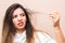 Hair problems. young woman in white shirt checking her britle, damaged, and split hairs against pink background