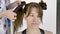 Hair stylist makes a young beautiful caucasian brunette`s hairstyle