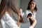 Haircare. Young Female Applying Hair Spray While Standing Near Mirror In Bathroom