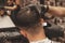 Haircut head in barbershop. Barber cuts hair on head of the client. The process of creating hairstyles for men. Selective focus.