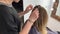 Hairdresser braiding woman`s hair in hairdressing salon.