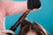 Hairdresser curling woman hair with iron curler.