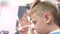 Hairdresser cuts bangs with scissors on boy`s head, face close-up side view.. Stylist`s hands.
