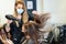 Hairdresser drying her client`s hair with a hairdryer wearing protective masks in a beauty centre.