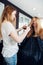 Hairdresser is engaged in trimming the split ends of long hair of positive young female client sitting in cape and
