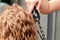 Hairdresser hands curl woman`s hair by curling iron