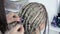 Hairdresser plaits braids on the blond girl`s head on a blurry background