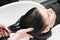 Hairdresser& x27;s hands wash long hair of brunette woman with shampoo in special sink for shampooing