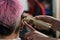 The hairdresser shaves the back of the head of a female client. Rear view of a woman with short pink hair in a