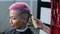 The hairdresser shaves the temple of a female client. Asian woman with short pink hair in barbershop.