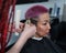 The hairdresser shaves the temple of a female client. Asian woman with short pink hair in barbershop.