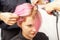 Hairdresser straights pink hair of woman by hair iron
