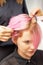 Hairdresser straights pink hair of woman by hair iron