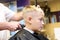 Hairdresser trimming blonde hair of young boy