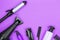 Hairdressing tools in black: hair dryer, combs, sprays, curling iron, hair clipper on a lilac background, space for text, flat lay