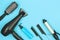 Hairdressing tools in black: hairdryer, combs, sprays, curling iron on a blue background, space for text, flat lay