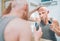 Hairless man touching his new style bald head haircut he made using an electric rechargeable Trimmer looking in bathroom mirror.